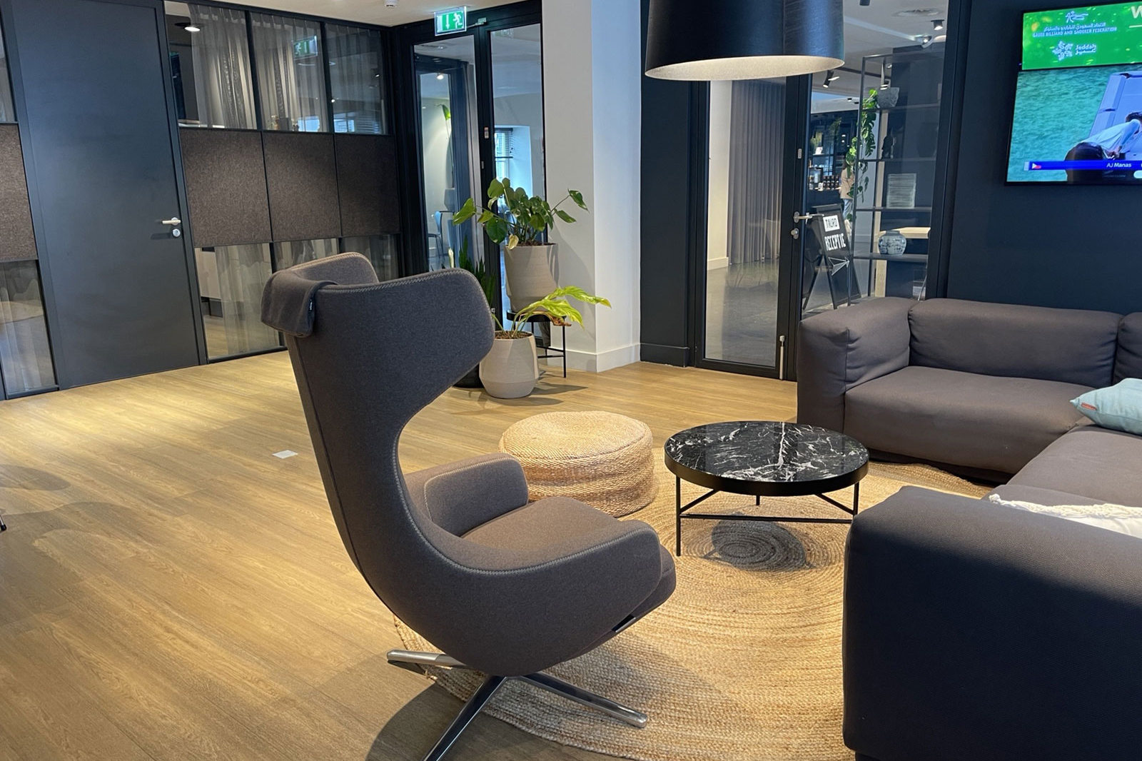 Een moderne kantoorruimte met een grote tv en een bank, met de eigenaren zichtbaar in de achtergrond.