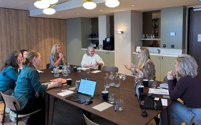 Een groep vrouwen zit rond een tafel in een vergaderruimte.
